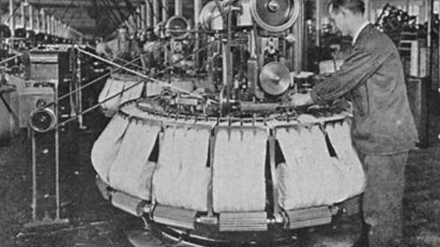 Old black and white picture of someone stood at a machine working on combs