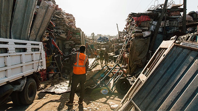 Someone working at a scrap metal yard wearing an orange high vis